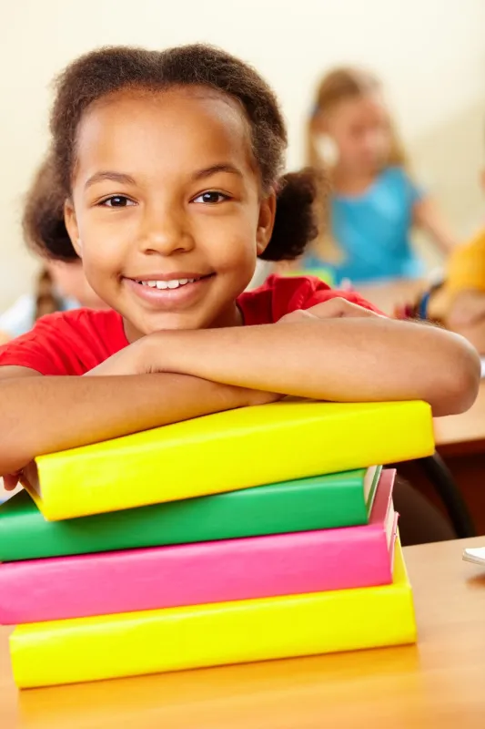 Happy pupil leaning on colourful school books